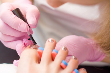 Obraz na płótnie Canvas Nail Care And pedicure concept. Closeup Manicurist hands in pink gloves is Painting gold Nail Polish On Client's toes. Woman In Beauty Salon.