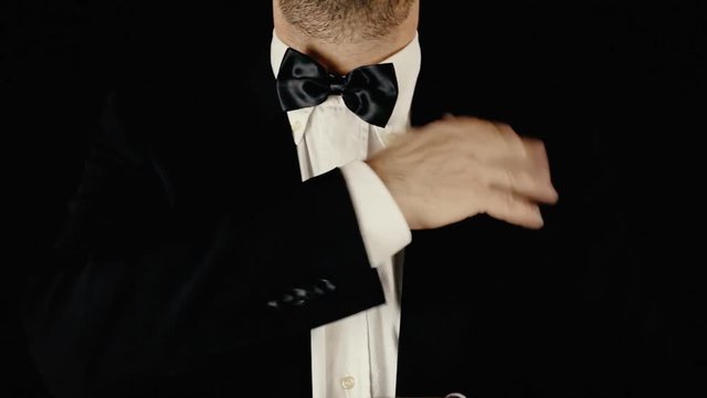 Lifestyle scene of a well-dressed man carefully adjusting his bow-tie.
