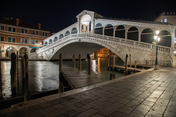Fototapeta na wymiar Night photo Rialto Bridge in Venice, Italy. Overview of the bridge illuminated by reflections on the water of the Grand Canal.