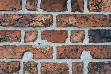 Wall of old cracked red brick with black inclusions.