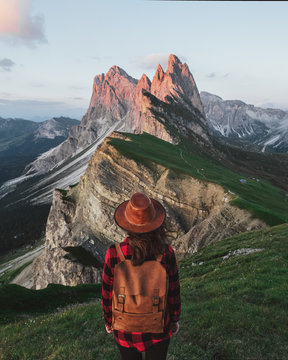 Young traveler girl with backpack and hat standing on mountains at sunset.