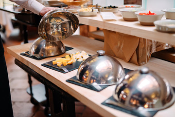 Cutting cheese on a metal bowl with a cap. Breakfast at the Hotel or restaurant.