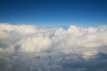 Fototapeta na wymiar Looking Out the Window of a Commercial Jet Down on a Bank of Enormous White Fluffy Clouds Heading North Up the East Coast of the United States toward Washington D.C. Late in the Afternoon
