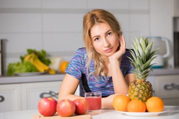 Pretty woman with fruits sitting at the table in kitchen, healthy food