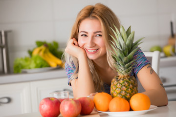 Pretty woman with fruits sitting at the table in kitchen, healthy food