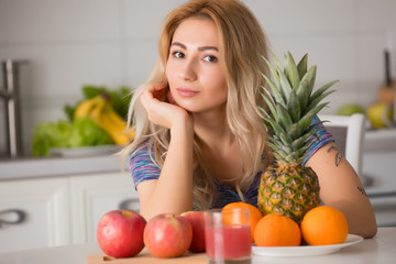 Pretty woman with fruits sitting at the table in kitchen, healthy food