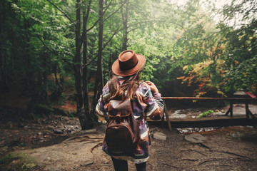 Stylish hipster girl in hat traveling in mountains. Young woman with backpack exploring and walking...
