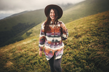 Portrait of happy young woman with backpack exploring mountains. Stylish hipster girl in hat...