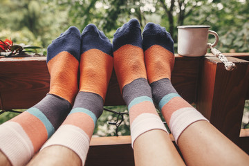 Stylish socks on couple legs and metal cup on wooden porch with view on woods in mountains. Happy...