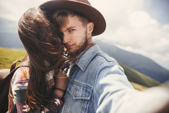 Happy hipster couple making selfie on top of windy mountains. Stylish sensual couple in love taking selfie photo and having fun. Travel together and Wanderlust concept.