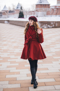 A beautiful girl in a red coat and a beret is walking along the Christmas street.