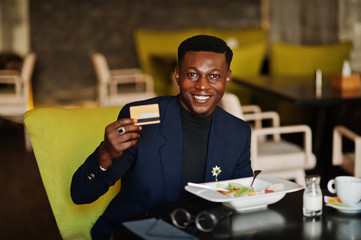 Fashionable african american man in suit sitting at cafe with credit card in his hand.