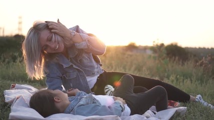 Mixed race family, european mother and asian daughter spending time in the park on sunset. They play lying on the ground tickle each other and smiling. Warm spring or summer season. B-roll slow motion