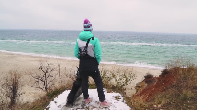 Young beautiful female walking with siberian husky dog on the beach at winter day, slow motion