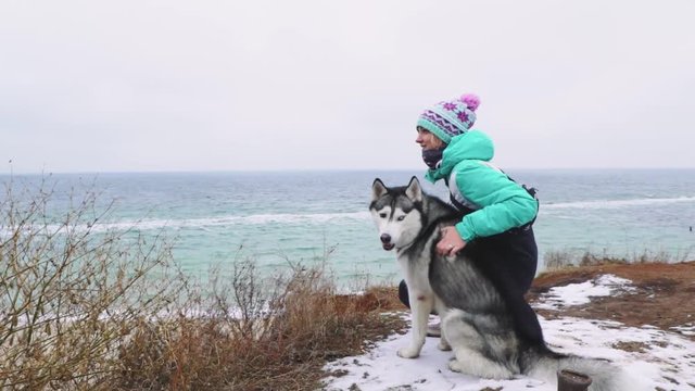 Young beautiful female walking with siberian husky dog on the beach at winter day, slow motion