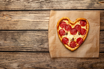 Heart shaped pizza on vintage wooden table background. The concept of romantic love for Valentine's Day