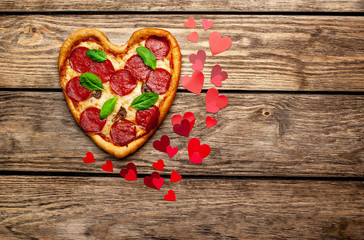Heart shaped pizza on vintage wooden table background. beautiful red paper saddles Concept of romantic love for Valentine's Day