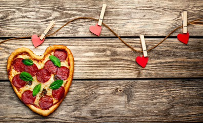 Heart shaped pizza on vintage wooden table background. beautiful red paper saddles Concept of romantic love for Valentine's Day