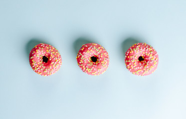 Donuts with pink icing and star sprinkles on the top on a blue background. Top view, flat lay.