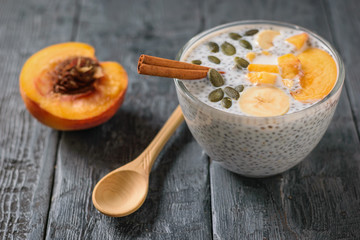 Half a peach and a wooden spoon next to a glass bowl of Chia seed pudding.