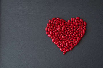 Fototapeta premium Red candy coated sunflower seeds in a heart shape on a gray slate background for Valentine’s Day