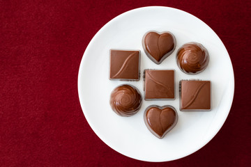 Assorted milk chocolate candy on a white plate on a red background for Valentine’s Day