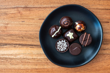 Assorted fancy chocolate candy on a rustic black plate on a wood background for Valentine’s Day