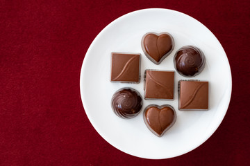 Assorted milk and dark chocolate candy on a white plate on a red background for Valentine’s Day