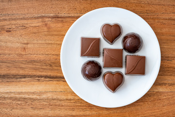 Assorted milk and dark chocolate candy on a white plate on a wood background for Valentine’s Day