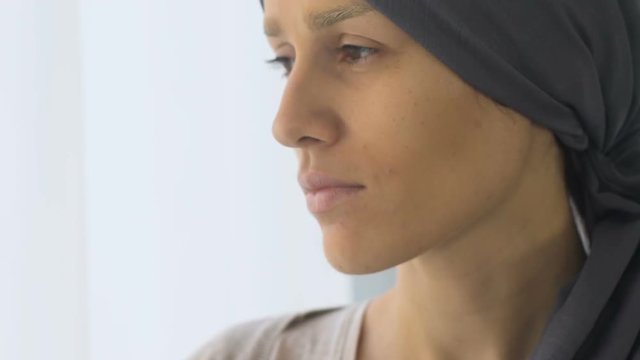 Upset cancer patient looking out window, weakened and depressed after chemo