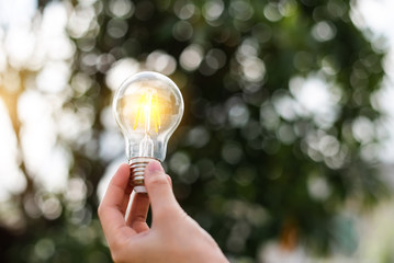 Hand holding light bulb with green background. idea solar energy in nature concept
