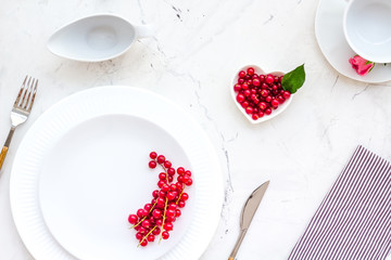 Elegant table setting with white plates, wineberry and floral decor on stone background top view