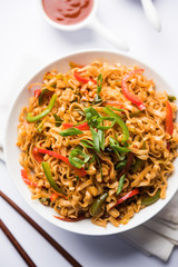 Schezwan veg noodles is a spicy and tasty stir fried flat Hakka noodles with sauce and veggies. served with chopsticks. selective focus