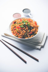 Schezwan veg noodles is a spicy and tasty stir fried flat Hakka noodles with sauce and veggies. served with chopsticks. selective focus