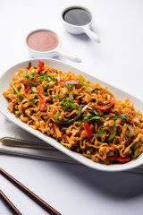 Schezwan veg noodles is a spicy and tasty stir fried flat Hakka noodles with sauce and veggies. served with chopsticks. selective focus