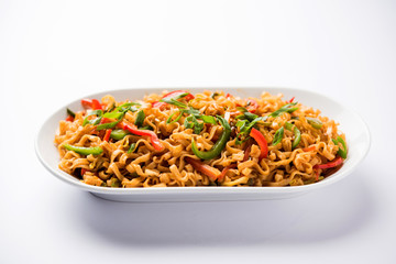 Schezwan veg noodles is a spicy and tasty stir fried flat Hakka noodles with sauce and veggies. served with chopsticks. selective focus