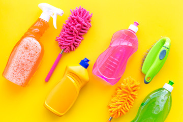 Housecleaning with detergents, soap, cleaners and brush in plastic bottles on yellow background top...