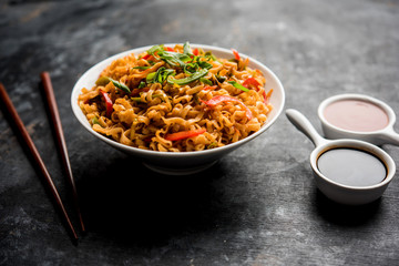 Schezwan veg noodles is a spicy and tasty stir fried flat Hakka noodles with sauce and veggies. served with chopsticks. selective focus