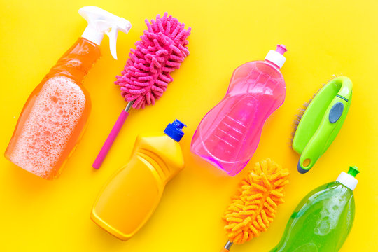 Housecleaning with detergents, soap, cleaners and brush in plastic bottles on yellow background top view mockup