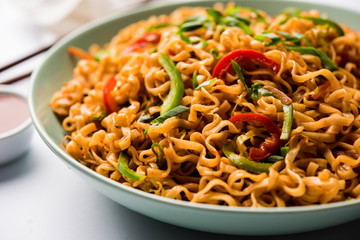 Schezwan veg noodles is a spicy and tasty stir fried flat Hakka noodles with sauce and veggies. served with chopsticks. selective focus