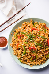 Schezwan veg noodles is a spicy and tasty stir fried flat Hakka noodles with sauce and veggies. served with chopsticks. selective focus
