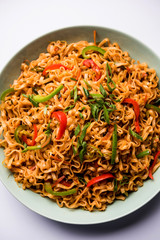Schezwan veg noodles is a spicy and tasty stir fried flat Hakka noodles with sauce and veggies. served with chopsticks. selective focus