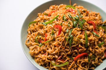 Schezwan veg noodles is a spicy and tasty stir fried flat Hakka noodles with sauce and veggies. served with chopsticks. selective focus