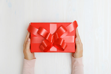 Close-up of a woman's hand giving a red box with a gift at the table. Top view. Concept of Valentine's Day and Christmas celebration