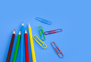 Office utensils supplies concepts, Colorful crayon pencils and multi-colored clips on blue background with copy space. View from above.