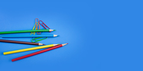 Web banner, poster wide template design concepts of stationery supplies, Colored crayon pencils and clips on blue background with copy space. Top view, Closeup.