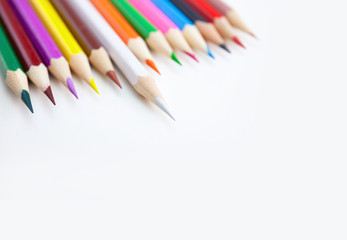A row of colored crayon pencils on the white desktop with selected focus on the white color tips with copy space. Top view, closeup.