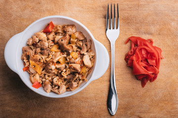 Asian pasta or noodles with vegetables and meat with spicy sauce on wooden Board with fork and ginger
