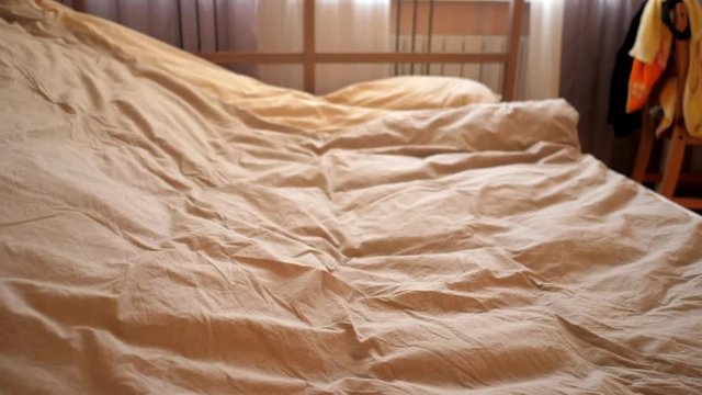 slow motion close view person shakes beige blanket like sail and puts on double bed in cozy bedroom in morning