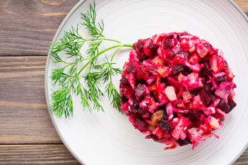 A portion of vinaigrette - a salad of boiled vegetables, sauerkraut and pickled cucumbers on a plate on a wooden table. National Russian dish. Top view